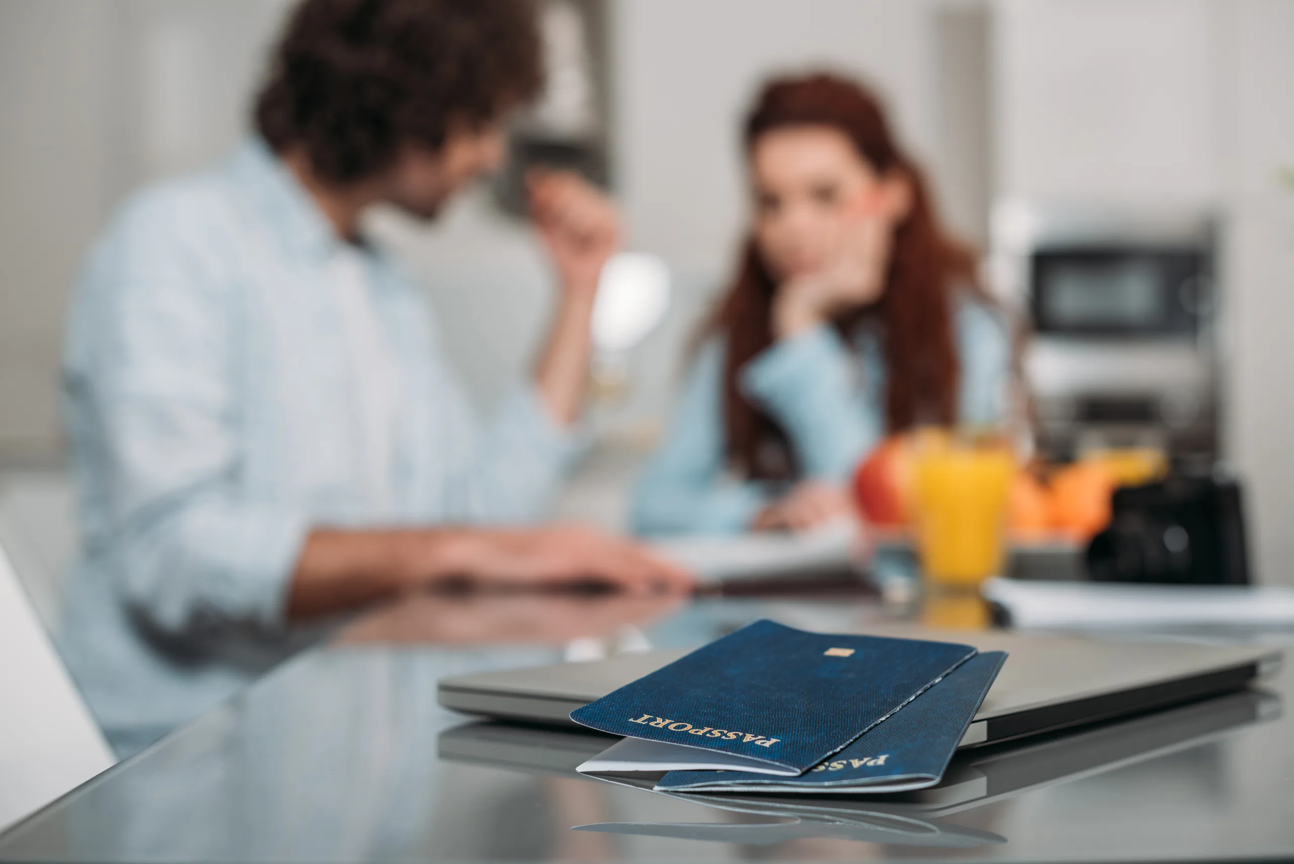 Two passports on a laptop, with a couple going through paperwork behind