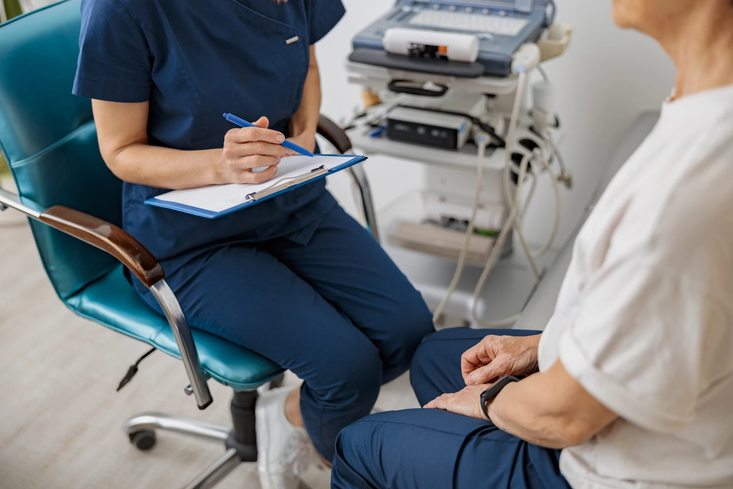 A clinician making notes on a clipboard while sitting with a patient