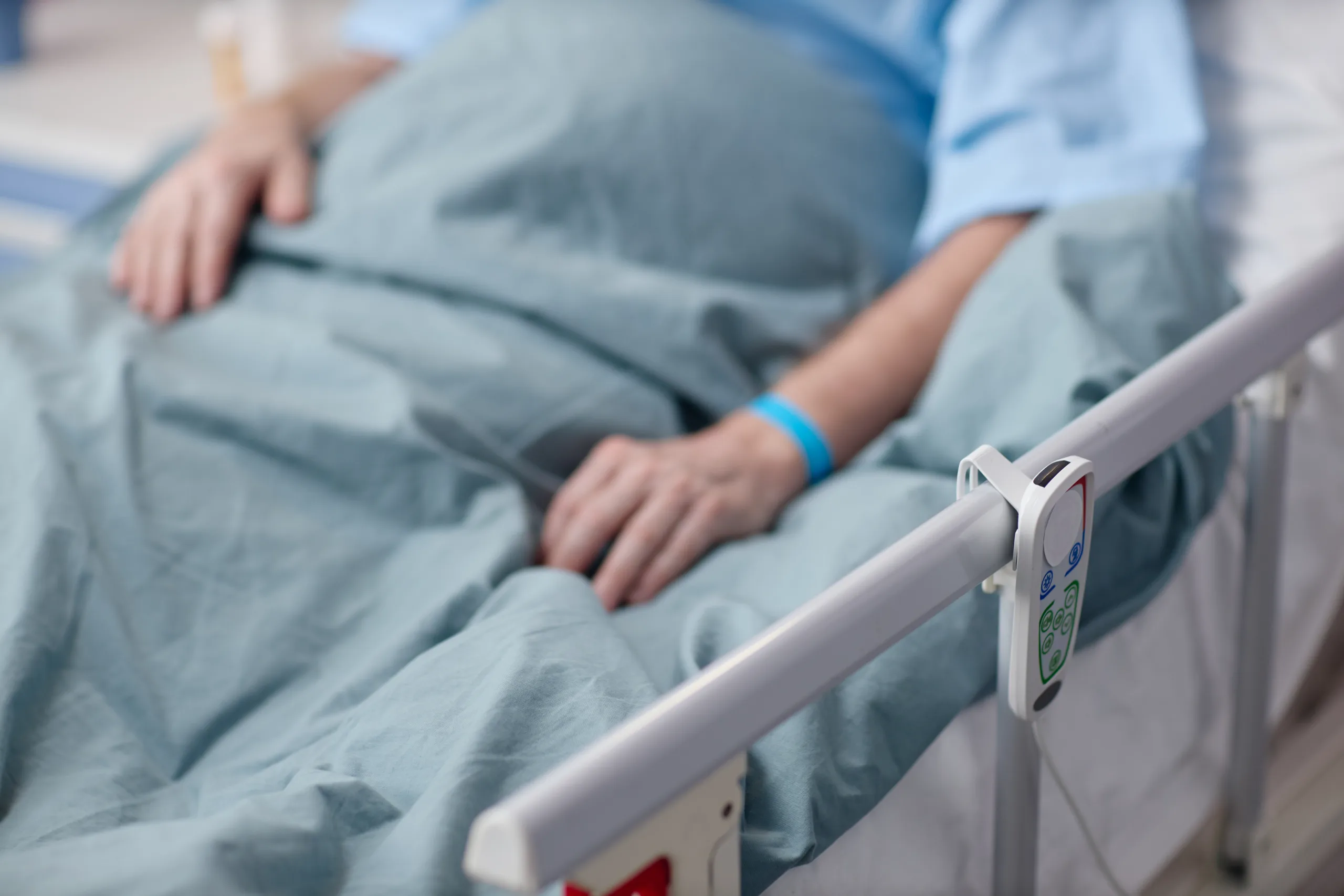 A patient resting, with a hand on the bed rail